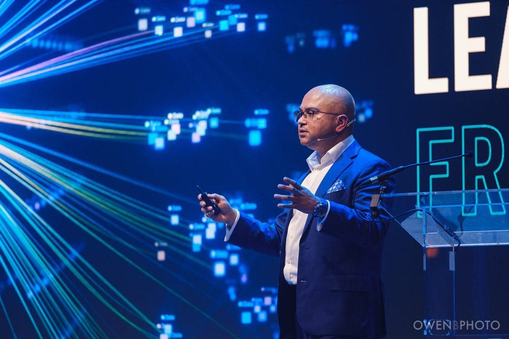 Speaker presenting against high-resolution LED screens at Vision Hall